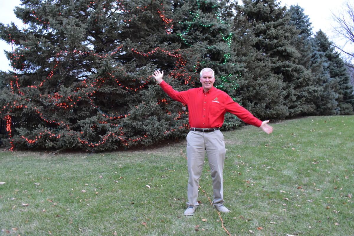 Mike Justak in 2018 posing in front of decorated trees.