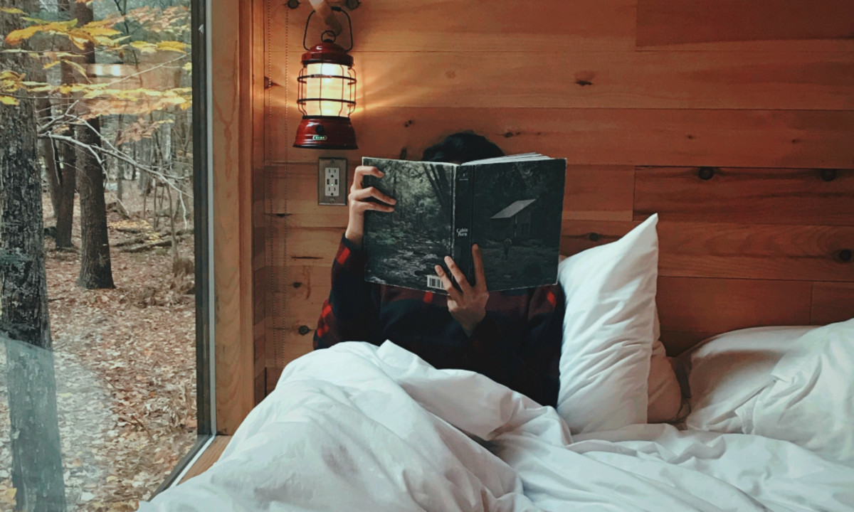 A person sitting in bed in a cabin, reading a book.